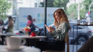 Neşeli kız cep telefonu sosyal medya izliyor rahat kafeteryada tek başına oturuyor. Cafe Break 'te cep telefonu mesajı okuyan gülümseyen kadın. Profesyonel garson bayan müşteriye taze kahve getiriyor..