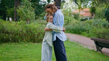 Sevgi dolu anne yeşillik parkında birbirine sarılıyor. Yetişkin kıvırcık kadın dışarıda küçük tatlı bir kızla iletişim kuruyor. Gülümseyen anne, sevimli kızıyla kucaklaşıyor ve eğleniyor. Annelik kavramı 
