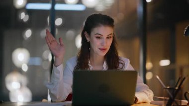 Laptop 'tan gece vardiyası videosu modern iş bürolarını kapatıyor. Gece online konferansta gülümseyen iş kadını konuşuyor. Pozitif kadın danışman sanal toplantıda işi tartışıyor.