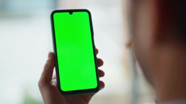 Ofisteki kromakey cep telefonunu yakın çekimde oynat. İş yerindeki yeşil ekran cep telefonunda iş uygulamasını izleyen bilinmeyen bir işadamı. Erkek parmağı akıllı telefon tarama uygulamasına dokunuyor.