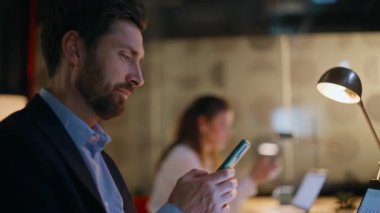 İş arkadaşlarını rahatlatmak, karanlık iş yerinde akıllı telefonlara göz atmak. İki yönetici fazla mesaiye ara vermek için cep telefonu kullanıyor. İş kadını lamba ışığında telefonları kaydırıyor