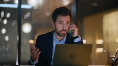 Çalışkan yönetici cep telefonuyla konuşuyor. Karanlık İş Merkezi 'nin iş yerinde dizüstü bilgisayar arıyor. Yakın plan. Profesyonel çalışan gece ofisinden arıyor. Sakallı iş adamı akıllı telefondan projeyi tartışıyor.