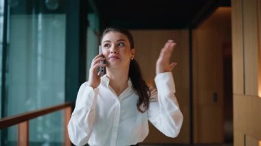 Ofiste çalışan mutlu bir çalışan, akıllı telefondan konuşuyor. Yakın plan. Gülümseyen iş kadını cep telefonunu arıyor modern koridorda yürüyor. Başarılı kadın yönetici koridorda cep telefonuyla haberleri paylaşıyor.