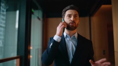 Mutlu iş sahibi cep telefonunu arıyor modern koridoru kapatıyor. Kendine güvenen iş adamı şirket koridorunda akıllı telefonla pazarlık yapıyor. Gülümseyen patron konuşuyor. Cep telefonu saati kontrol ediliyor..