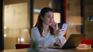 Kadın serbest çalışan cep telefonuna mesaj atıp karanlık bir yerde oturuyor. Gülümseyen iş kadını gece ofisinde akıllı telefon mesajı okuyor. Rahatlamış yönetici cep telefonunda sosyal medyaya göz atıyor.