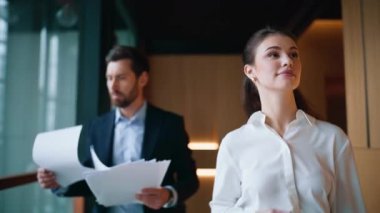 İş ortakları koridorda dokümanlarla yürüyorlar. Yakın plan. Gülümseyen iş kadını mutlu iş adamına cep telefonundan harika haberler veriyor. İki meslektaş iş başarısını kutluyor, kağıt atıyorlar.