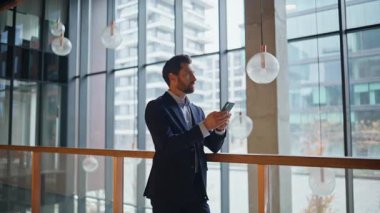 Ofis koridorunda tek başına akıllı telefonu tutan zarif bir çalışan. Sakallı işadamı, modern iş merkezinin içindeki cep telefonuna bakıyor. Gülümseyen adam telefon mesajını okuyarak yakınlaştır.