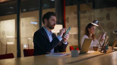 Ofisteki iş arkadaşları iş yerinde cep telefonu kullanıyorlar. Ciddi iş kadını gece işyerinde akıllı telefonlara bakıyor. Profesyonel yöneticiler lamba ışığı altında cep telefonlarına bakıyor.