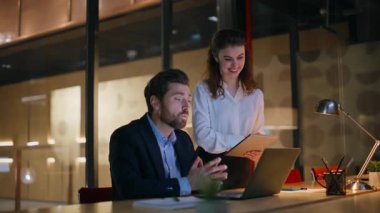 Şirket video ekibi, karanlık modern ofisten laptop 'ı arıyor. İnternetteki konferansta kameradan bahseden iki meslektaşım fazla mesai yapıyor. Gülümseyen mutlu iş arkadaşları akşam iş yerindeki sanal buluşmada selamlıyorlar..