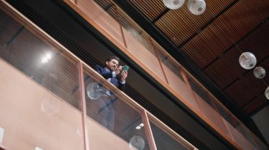 Gülümseyen bir çalışan cep telefonuyla mesajlaşıyor parmaklıklara yaslanıyor cam ofis balkon manzarası. Koridorda cep telefonu mesajı okuyan mutlu bir işadamı. Modern iç mekanlarda sakallı, akıllı telefonları tarayan bir CEO..