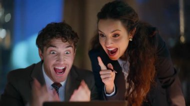 Heyecanlı iş arkadaşları karanlık ofisin kapanışında sevinçle dizüstü bilgisayar izliyorlar. Mutlu iki meslektaş gece işyerinde iş başarısını kutluyor. Duygusal partnerlere beş başarı şansı