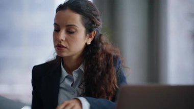 Odaklanmış kadın, ofis içi portrede dizüstü bilgisayarlı masa başında oturan kağıtlara bakıyor. Belgelerle yakından ilgilenen ciddi bir yönetici. Kaşlarını çatan iş kadını sadece grafiklerle ilgili bilgileri karşılaştırıyor. 