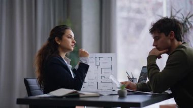 Yaratıcı ajans ofisinde kadın, erkek müşteriyle mimari planı tartışıyor. Profesyonel bayan, özel kabine toplantısındaki adama daire tasarımını tavsiye ediyor. Müşteri planlarını inceliyor 