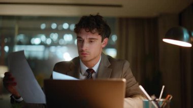 Odaklanmış adam, şirketlerin iş yerinde çalışan belgeleri inceliyor. Tatminsiz iş adamı dizüstü bilgisayarda hata arıyor. Stresli adam kağıtları fırlatıyor. İş sorunu yüzünden üzgün.