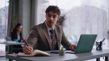 Şirket çalışanı, modern işyerindeki defter defterine fikirleri not ederek proje yaratıyor. Başarılı iş planı üzerine düşünen gülümseyen bir iş adamı. Birlikte çalışmada dizüstü bilgisayarda çalışan pozitif profesyonel