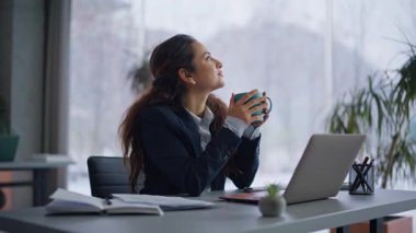 Rahatlamış esmer dinlenme odası panoramik pencereye yakın görünüyor. Hayalperest iş kadını sıcak bir bardak sıcak içecek alıyor. Sakin bayan yönetici sabah iş yerinde mola veriyor.