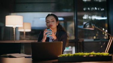 Akşam iş kadını lamba ışığı altında oturup espresso içiyor. Özel kabinede fazla mesai yapan yorgun bayan yönetici. Kadın kahve molası veriyor. Dizüstü bilgisayar ekranı.