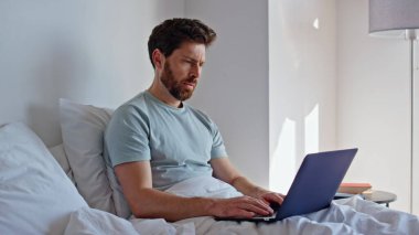Stresli yönetici yatak odasında çalışıyor, sabahları bilgisayar ekranına bakıyor. Laptop kullanan esmer serbest yazar dosyada hata buldu. Sinirli adam güneş ışığı odasında dijital cihaz kapağını kapatıyor. 
