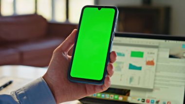 İşçi, iş yerindeki fotoğraflara bakarak yeşil ekran cep telefonunu yakınlaştırıyor. Kimliği belirsiz erkek elleri krom tuşlu akıllı telefon internette sörf yapıyor. Ofisteki cep telefonunun taklidini yapan erkek parmakları.