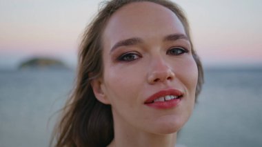 Okyanusun alacakaranlığında poz veren esmer kadın. Pembe deniz ufkunda kendine güvenen sakin, güzel bir kadın portresi. Parlak model akşam kumsalında meltemin tadını çıkarıyor. Deniz doğumu