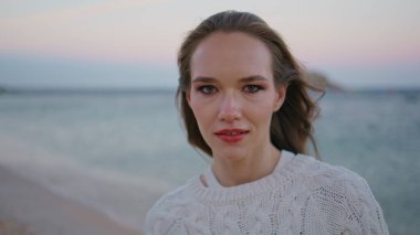 Akşam kumsalındaki portre modeli kendinden emin bir şekilde kameraya bakıyor. Sakin sakin kadın gün batımında kıyıda dikiliyor. Ufuk çizgisine yakın. Alacakaranlık ufkunda poz veren tasasız kadın. Deniz tatili kavramı