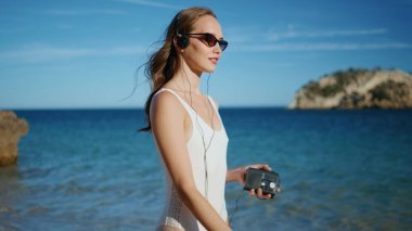 Okyanus kıyısında kaset çaları dinleyen bir kadın. Rahatlamış bayan kulaklıklarla müzik dinliyor güneşli tropikal plajlarda yürüyor. Mutlu bayan tatilci kaygısız yaz tatilinde ıslak kuma basıyor..