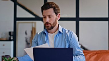 Sakallı iş adamı evde kontrat okuyor. Kapanış mutlu adam modern dairede kağıtları kontrol ediyor. Başarılı esmer yönetici düşünme projesi. Uzaktan kumanda yöneticisi bilgisayarda tek başına çalışıyor