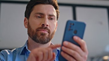 Evdeki oturma odasında akıllı telefondan SMS okuyan neşeli bir adam. Gülümseyen genç işadamı cep telefonunun ekranına bakıyor. Mutlu yakışıklı adam rahat bir dairede alışveriş uygulamasına bakıyor. 