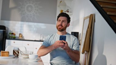 Romantik adamın elinde akıllı telefon var. Mutfağın iç tarafında samimi bir şekilde oturuyor. Sabahları cep telefonu kullanan yakışıklı adam kahvaltı saatinde mesaj bırakıyor. Rahatlamış serbest çalışan cep telefonuna tek başına mesaj atıyor.