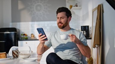Akıllı telefondan SMS okuyan gülümseyen adam rahat bir mutfak kapanışı yapıyor. Elinde çay fincanıyla cep telefonu kullanan yakışıklı, tıraşsız adam. Rahatlamış serbest çalışan işten önce cep telefonuna mesaj atıyor. 