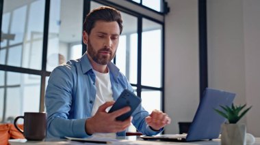 Dizüstü bilgisayarda çalışan gülümseyen iş adamı cep telefonu uyarısını kontrol ediyor. Sinirli adam masadaki kötü mesaja tepki veriyor. Duygusal açıdan deli bir adam stresli ve sorunlu. 