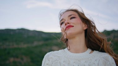 Kumral, rüzgarlı bir sabahın keyfini çıkar. Yeşil tepelerin önünde dikilirken. Alacakaranlık doğasında poz veren güzel genç bir kadın portresi. Tasasız model, rahat kazak giyiyor. Dışarıdaki kameraya bakıyor.