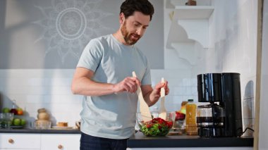Mutfağa yakın bir yerde salata hazırlayan olumlu adam. Kaygısız neşeli adam hafif dairede sebze pişiriyor. Gülümseyen esmer erkek tek başına lezzetli yemekler yapıyor. Mutfak konsepti 