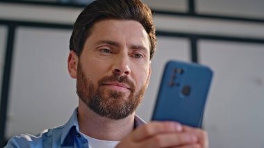 Ofisteki akıllı telefon ekranında sohbetiniz kutlu olsun. Gülümseyen adam iş yerinde cep telefonundan mesaj okuyor. Genç işadamı bankacılık uygulamasından memnun