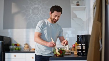 Tasasız adam evde salata hazırlıyor. Yakın plan. Pozitif erkek, sağlıklı yemek hazırlıyor. Elinde tahta spatula tutan genç adam tek başına yemek yapıyor. Vejetaryen beslenme konsepti 