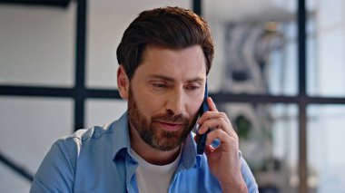 Modern ofis portresinden pozitif patron cep telefonunu arıyor. Gülümseyen sakallı bir adam akıllı telefondan konuşuyor. Dairenin iş yerini yakından dinliyor. Neşeli iş adamı cep telefonu görüşmesini bitirdi