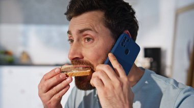 Sabahçı adam akıllı telefondan arıyor ve çikolatalı sandviç yiyor. Orta yaşlı yakışıklı işadamı cep telefonundan konuşup açık mutfakta en sevdiği yemeğin tadını çıkarıyor. Neşeli adam dinleniyor 