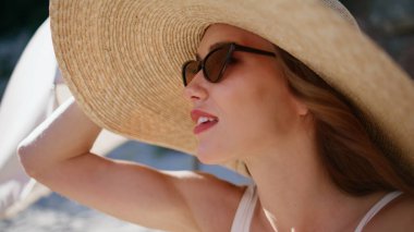 Hasır şapkalı kadın okyanus ufkuna bakıyor güneş panelinde oturuyor. Güneş gözlüğü takan şık bayan güneşli kumsalda dinleniyor. Güzel esmer, deniz manzarasının tadını çıkarıyor..