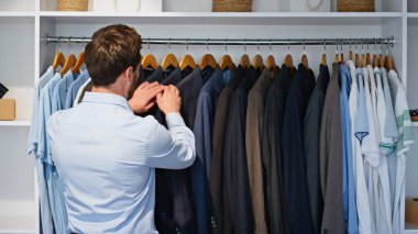 Yetişkin menajer spor ceketi seçiyor. Lüks bir dairede ahşap askılık takıyor. Takım elbiseli sakallı adam tek başına büyük modern gardıroba ayna yansıması olarak bakıyor. İş adamları yaşam tarzı kavramı 