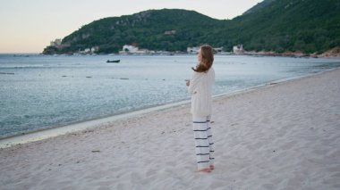 Rüzgarlı sahilde okyanus ufkuna bakan hayalperest kadın. Romantik bayan turist, sabah deniz manzarasının kumsalda tek başına durduğunu düşünüyor. Deniz dalgalarından zevk alan güzel bir bayan. Kıyı şeridinde dinleniyor..
