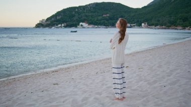Deniz manzarası seyreden bir kız. Rahat bir kadın, güzel bir okyanus manzarası seyrediyor kumlu sahilde tek başına duruyor. Romantik bayan gezgin yaz tatilini deniz kıyısında geçiriyor..