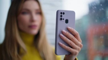 Sarışın cep telefonuyla sosyal medya izliyor. Dairenin penceresinin önünde dikiliyor. Gülümseyen kadın evde akıllı telefon mesajı okuyor. İçerideki cep telefonunda internet içeriğine göz atan mutlu genç iş kadını