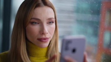 Ofis penceresinde cep telefonuyla mesajlaşan portre kadını. Gülümseyen genç sarışın cep telefonunun kapanışında sosyal medya içeriğini araştırıyor. Mutlu bayan evde güzel akıllı telefon mesajları okuyor..