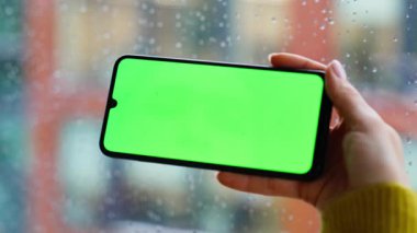 El dinleme cihazı, cep telefonu çevrimiçi uygulama, daire pencerelerine yakın çekim. Yatay yeşil ekran akıllı telefon tutan kimliği belirsiz bir kadın. Chroma Key Phone 'da sosyal medyayı izleyen serbest çalışan bir kadın..