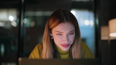 Gülümseyen programcı dizüstü bilgisayarı karanlık çalışma alanına yakın oturuyor. Gece işyerinde bilgisayardan e-posta okuyan mutlu bir iş kadını. Memnun kadın yönetici fazla mesai yaparak başarıyı düşünüyor..