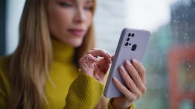 Yakından bakan iş kadını yağmurlu pencerenin yanında duran SMS 'leri sevindiriyor. Portre gülümseyen kadın akıllı telefondan gelir bildirimi alıyor. Heyecanlı bayan serbest yazar telefon mesajı okuyor. Çok mutlu..