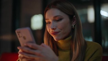 Karanlık dairede akıllı telefondan mesaj atan bir kadın. Portre gülümseyen iş kadını gece ofisinde cep telefonuna mesaj atıyor. Gevşemiş sarışın kadın cep telefonuyla internet iletişiminin tadını çıkarıyor..