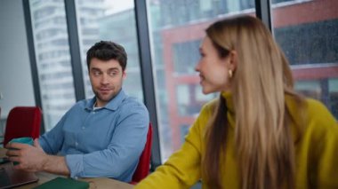Ofiste açık alanda yakın plan çekimde aynı fikirleri paylaşan iki çalışan. Elinde kahve fincanı tutan olumlu bir adam gülümseyen kadın meslektaşla konuşuyor. Takım yöneticileri pencere kenarında oturarak dostça iletişimi severler