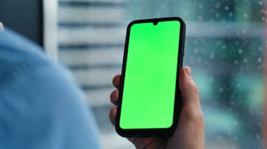 Erkek parmakları dairenin penceresinin yanında duran yakın plan cep telefonu. Ofiste yeşil ekran cep telefonu kullanan kimliği belirsiz bir işadamı. Chroma Key akıllı telefonunda sosyal medya uygulamasını izleyen adam..