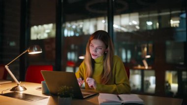 Çok çalışan bir kadın, gece vardiyasında bilgisayarın kapağını kapatıyor. Yorgun iş kadını, karanlık ofis yerinde dizüstü bilgisayardaki işini bitiriyor. Motivasyonsuz bayan işyerinde oturuyor ve profesyonel yorgunluk yaşıyor..